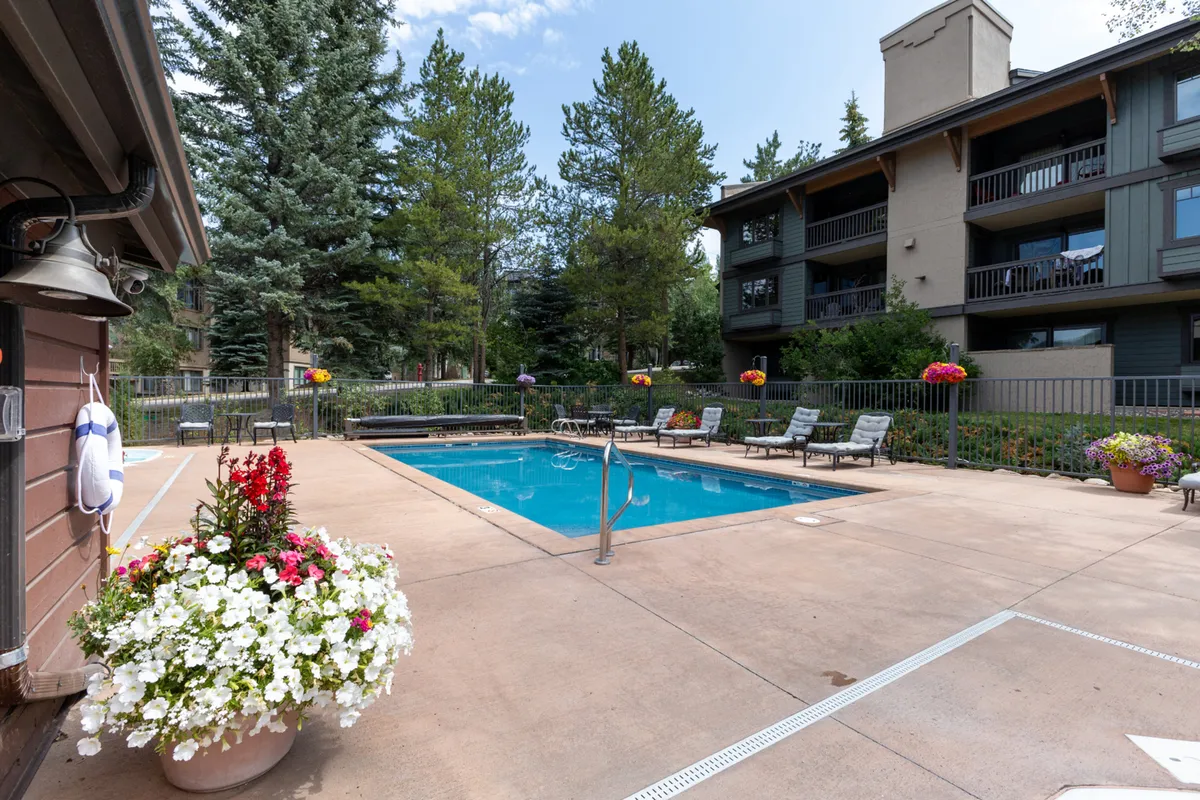 A relaxed exterior view of the swimming pool with flower pots and lounge chairs against the building facade, capturing the inviting communal outdoor space available to guests.