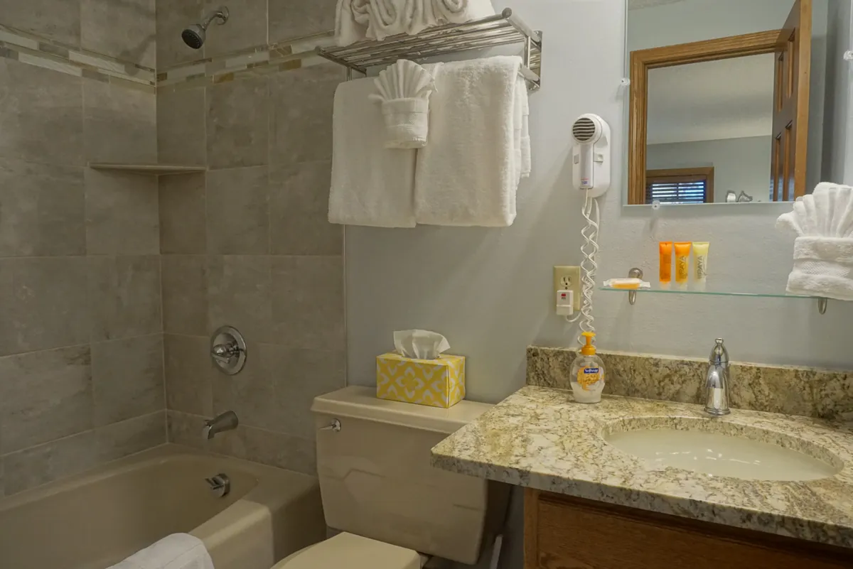 This bathroom interior features a granite countertop, a bathtub, plush towels, and elegant toiletries. The spa-like ambiance is enhanced by inviting lighting, creating a relaxing and practical space for self-care routines.