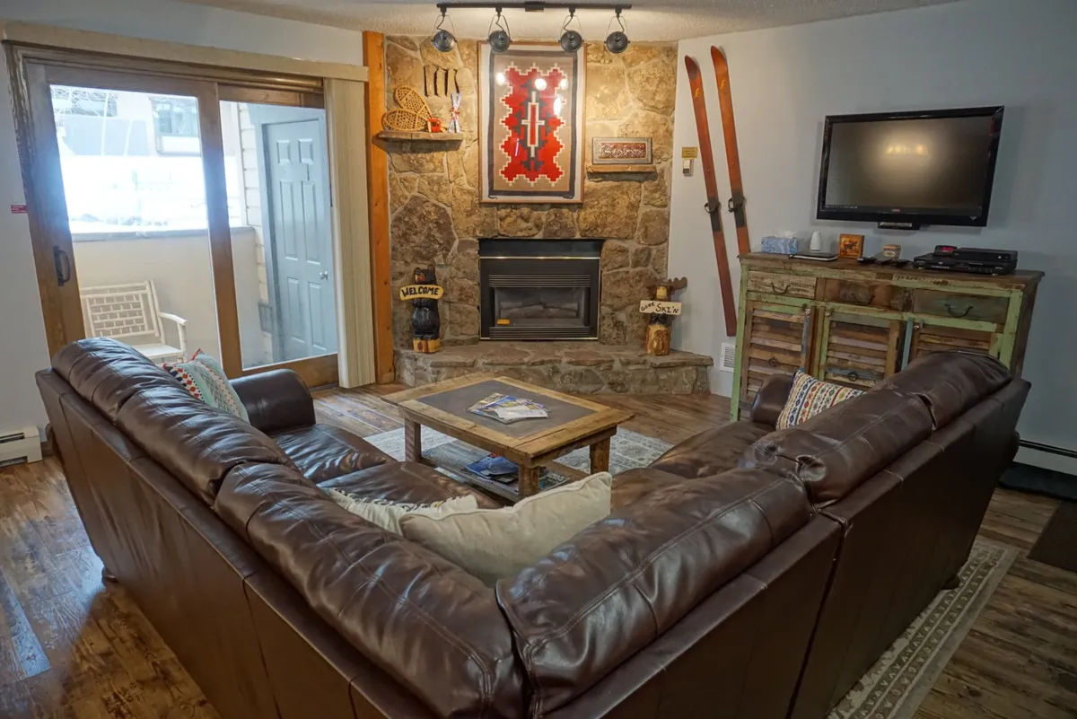 A welcoming lounge area featuring a stone fireplace, a leather sofa, and a wooden coffee table surrounded by rustic decor. The scene exudes warmth and comfort, ideal for gatherings after a day of adventure.