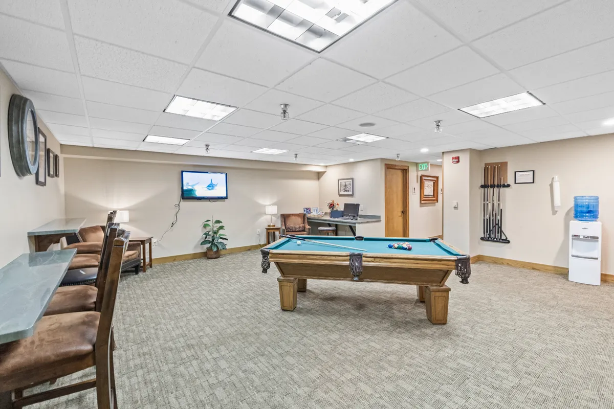 A bright, welcoming clubhouse interior with a pool table, seating area, and television, encouraging social activities and family fun. The space is clearly designed for communal enjoyment, echoing the section’s details about family-friendly clubhouse amenities.