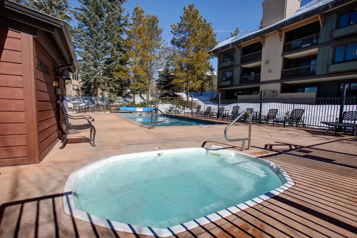 An inviting outdoor scene featuring a hot tub adjacent to a swimming pool, surrounded by trees and lounge chairs. The atmosphere is one of relaxation and social enjoyment, ideal for both unwinding after a day of activities and gathering with friends or family.