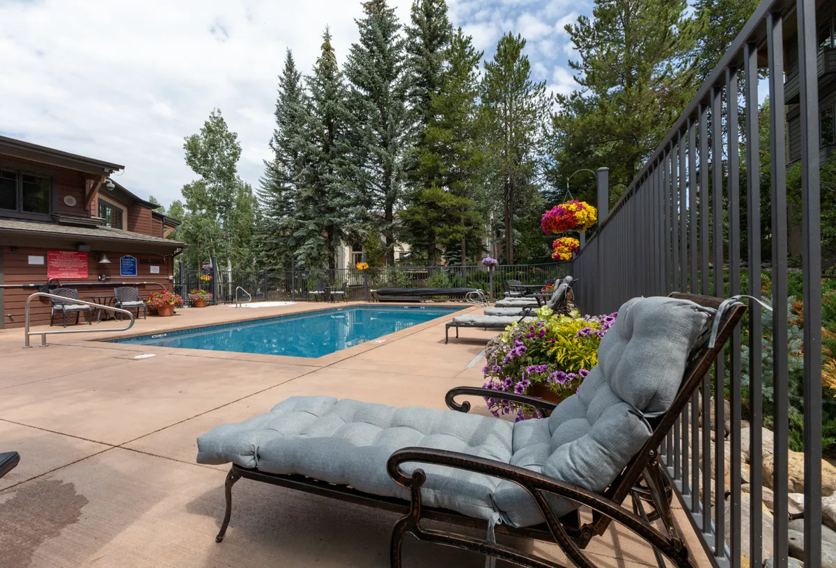 An inviting exterior view of the resort-style swimming pool surrounded by lounge chairs and vibrant flower arrangements. The scene is tranquil, highlighting multiple seating options and easy access for guests of all ages. The pool area is shown in soft, attractive lighting, ideal for both daytime and evening relaxation.