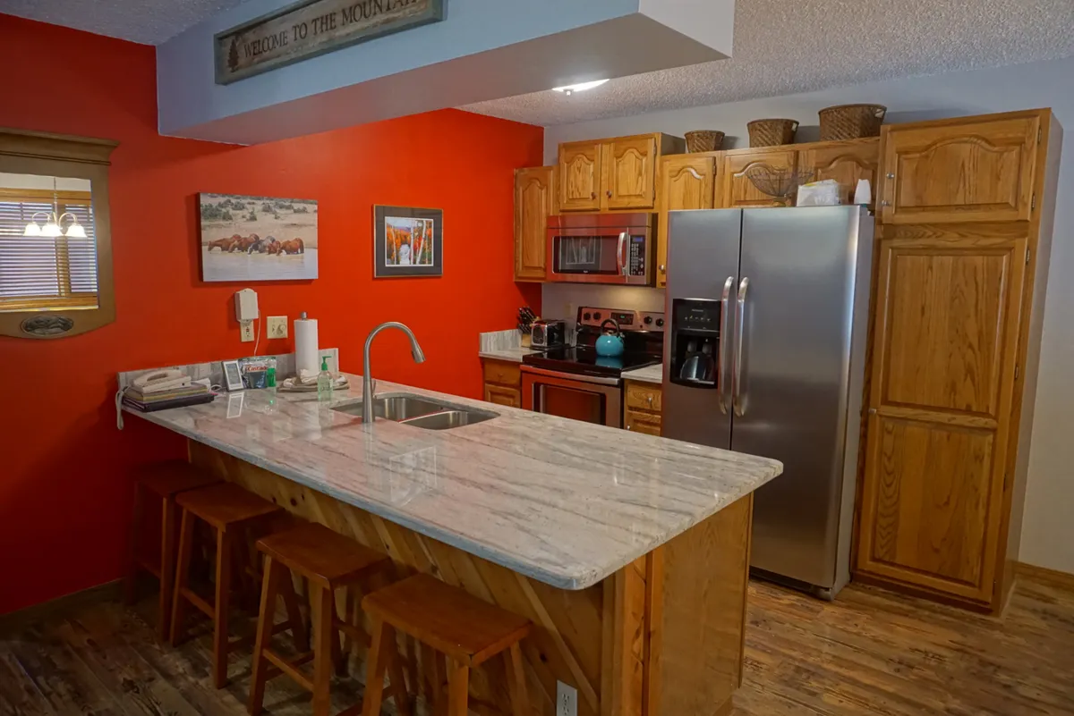 A functional kitchen with granite countertops, bar stools, red accent wall, and visible appliances. This image foregrounds the peninsula seating and the kitchen's modern amenities.