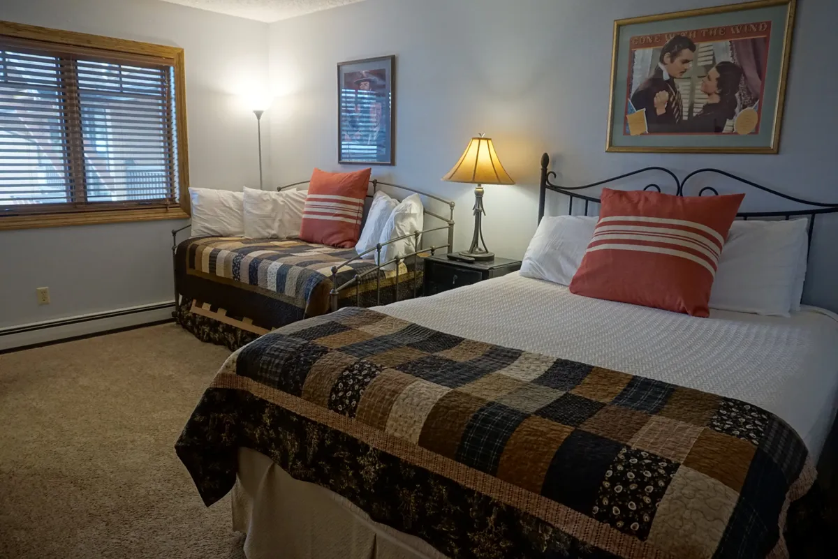 This image features two beds with patchwork quilts, a table lamp, and framed artwork, creating a comforting and inviting space. The arrangement is ideal for flexible sleeping needs, whether for kids or adults. Warm lighting and soft bedding enhance the tranquil mood of the room.