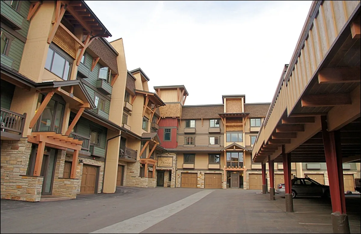 A charming exterior shot of the condo building, featuring wooden beams, stone facade, balconies, and large windows. The open courtyard suggests year-round vibrancy and accessibility, ideal for families walking to and from nearby attractions.