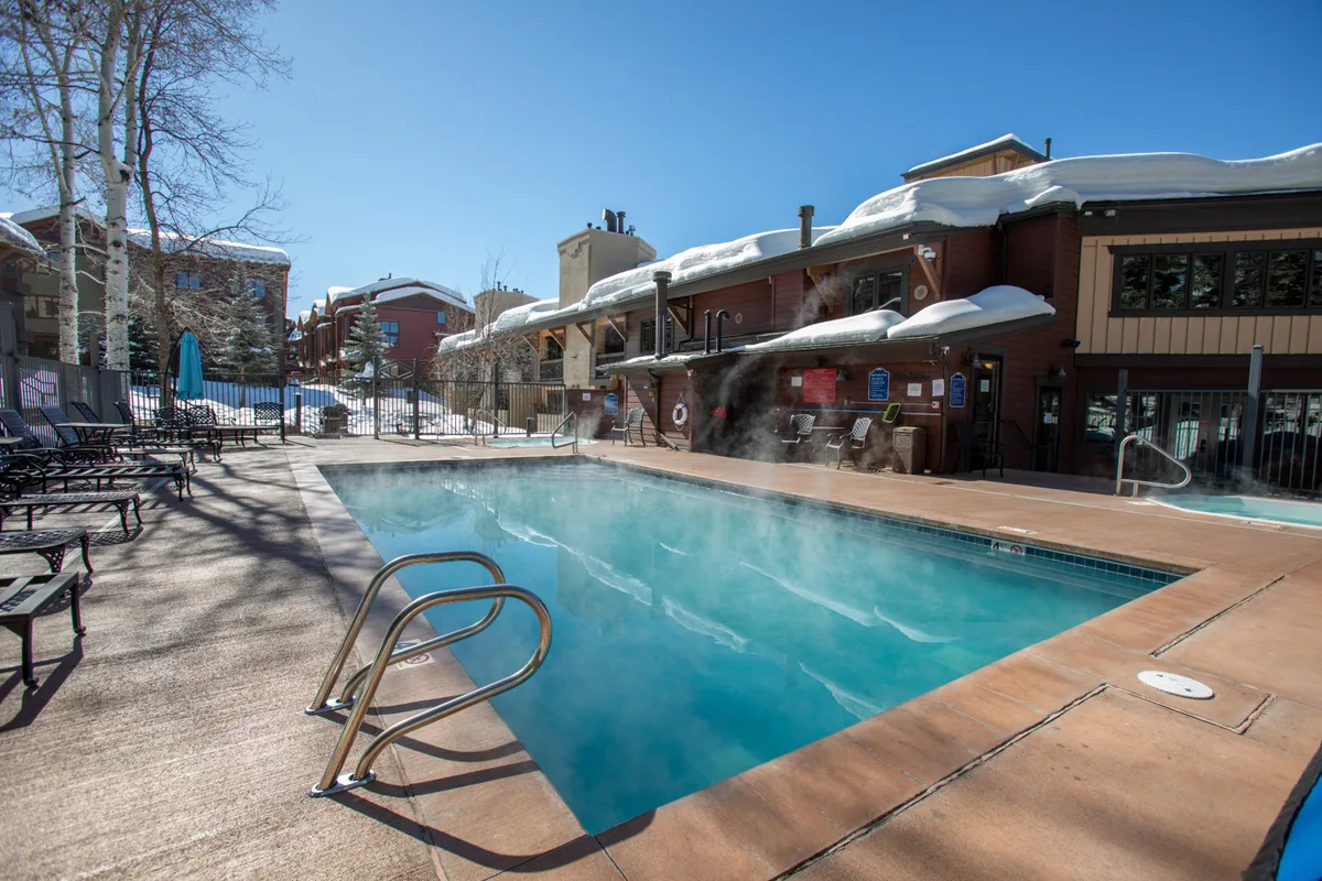 A heated swimming pool surrounded by lounge chairs, set against a backdrop of snow-covered ground. The pool area is inviting, with steam rising from the water and plenty of seating for guests to relax, reflecting both leisure and year-round accessibility.