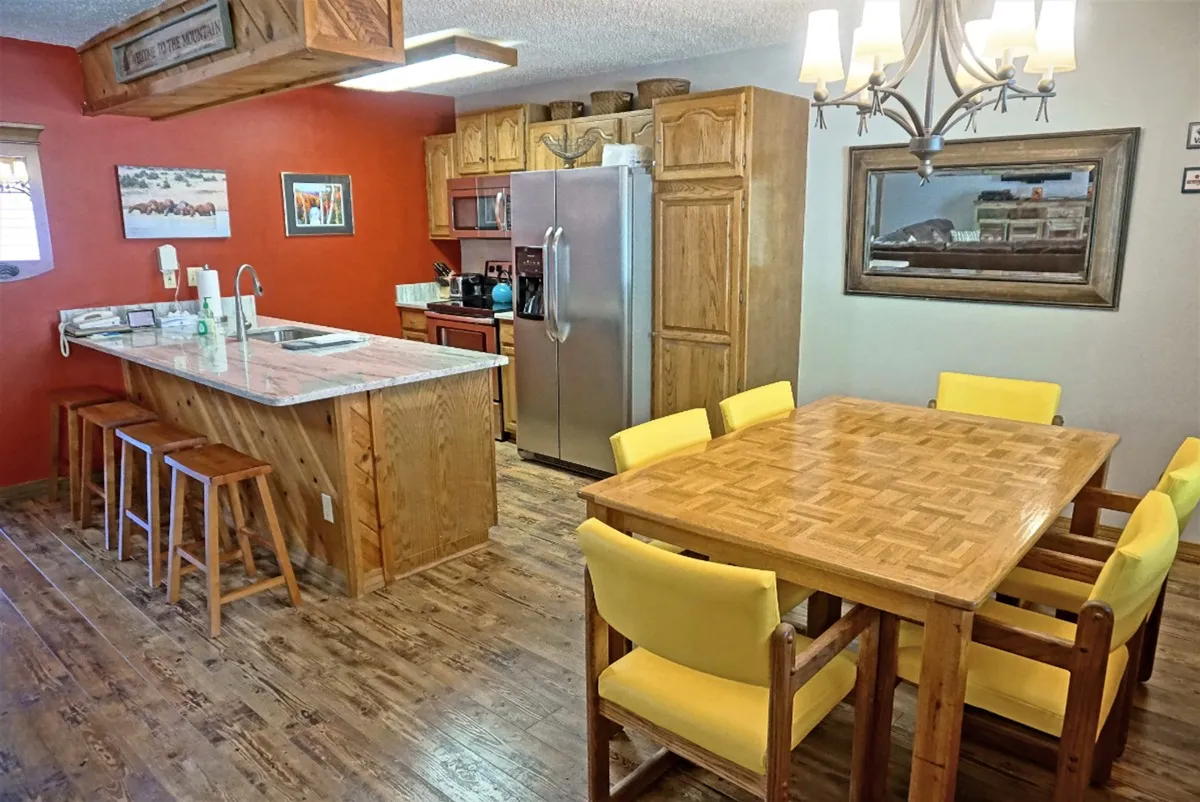 A cozy and inviting kitchen and dining area featuring a central kitchen island and a welcoming dining table beneath a warm chandelier. The space is set up for shared meals, group gatherings, and the convenience of in-condo dining.