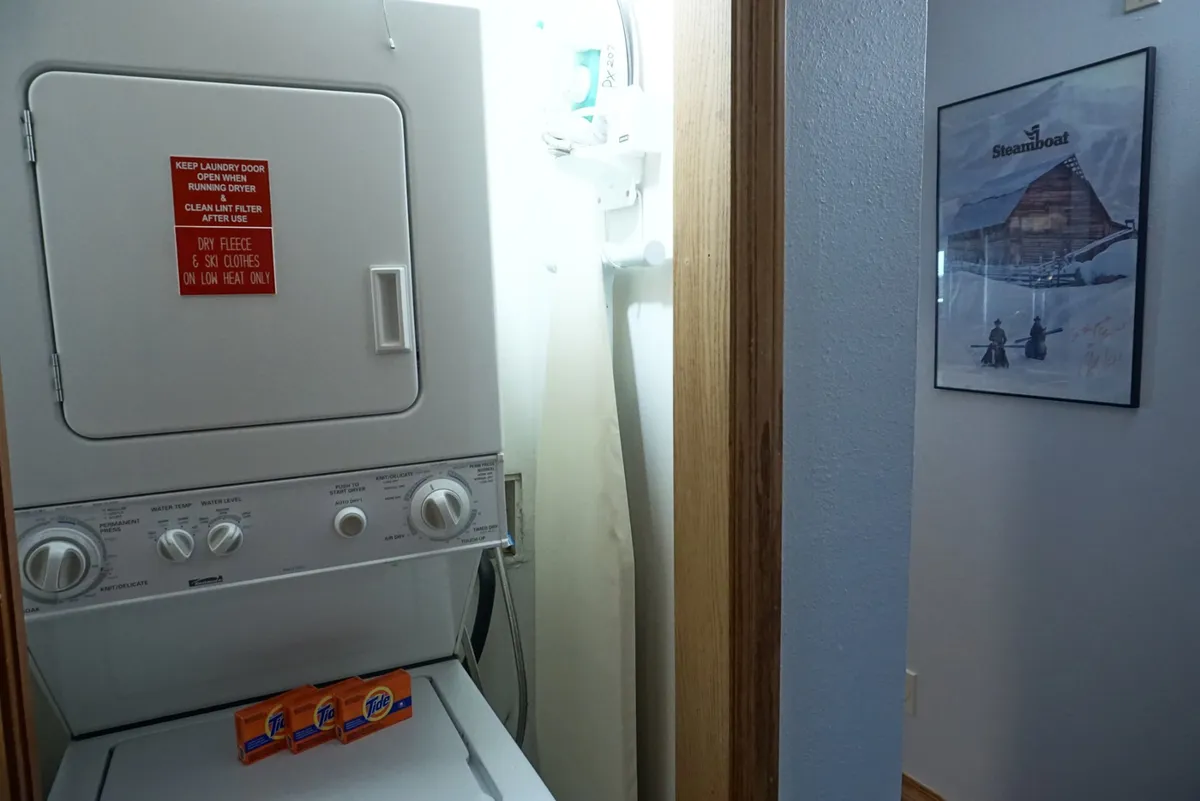 An in-unit laundry space with washer, dryer, laundry detergent, and framed local art, offering both practicality and a touch of local character for guests staying longer.